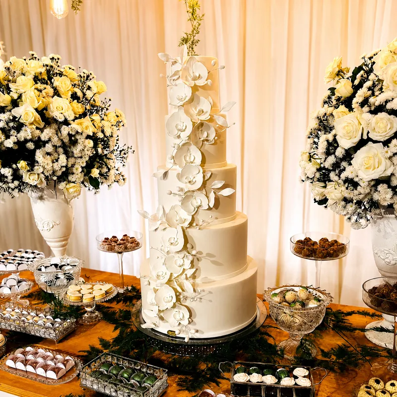 Bolo de casamento branco de cinco andares com orquídeas na mesa de doces